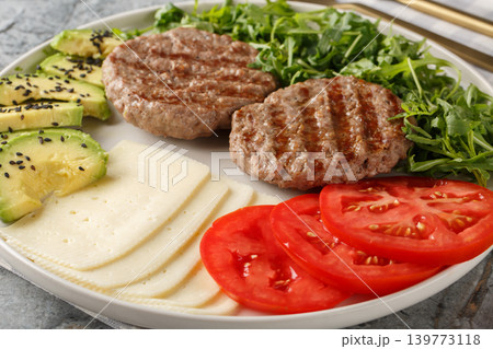 Low-carb burger with cheese, avocado, grilled patty, tomatoes and arugula close-up on a plate. Horizontal Low-carb burger with cheese, avocado, grilled patty, tomatoes and arugula close-up on a plate. Horizontal 139773118