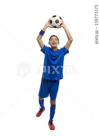 A happy young Indonesian southeast asian soccer player in a blue uniform holding a football above his head, ready for a throw-in or celebrating. Isolated on a white background A happy young Indonesian southeast asian soccer player in a blue uniform holding a football above his head, ready for a throw-in or celebrating. Isolated on a white background 139773173