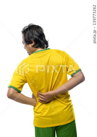 A Indonesian southeast asian man in a yellow and green sports uniform holding his lower back in pain, suggesting a sports injury or muscle strain, isolated on a white background A Indonesian southeast asian man in a yellow and green sports uniform holding his lower back in pain, suggesting a sports injury or muscle strain, isolated on a white background 139773262