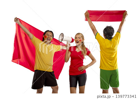 A diverse group of three Indonesian southeast asian enthusiastic sports supporters, two men and a woman, cheering excitedly while holding red flags and a megaphone, isolated on a white background A diverse group of three Indonesian southeast asian enthusiastic sports supporters, two men and a woman, cheering excitedly while holding red flags and a megaphone, isolated on a white background 139773341