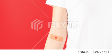 Blood donation. Human hands with plaster heart on arm against red background. Hematologic disorders such as anemia, sickle cell disease, hemophilia, leukemia and ITP. 139773371