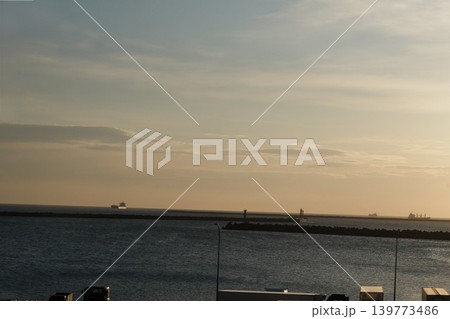 日の出前の穏やかな海に浮かぶ遠くの貨物船と防波堤の風景 139773486