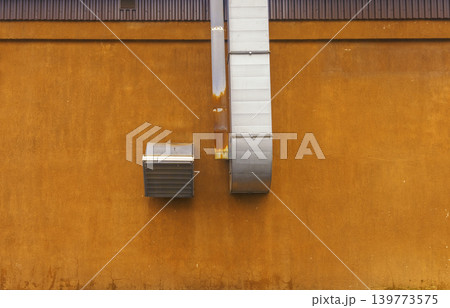 Exposed metal ductwork and ventilation fixtures set against vividly colored industrial style wall surface 139773575