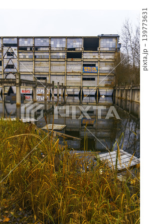 Urban decay with water reflections. Crumbling modular block mirrored in water with reeds foreground Urban decay with water reflections. Crumbling modular block mirrored in water with reeds foreground 139773631