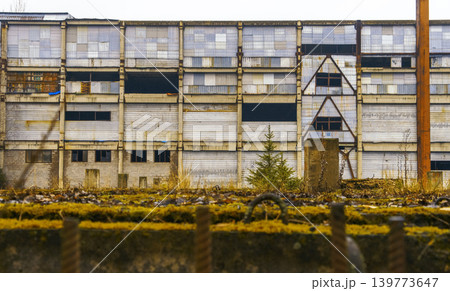 Old empty building overtaken by nature. Neglected city block featuring broken windows and overgrown fences Old empty building overtaken by nature. Neglected city block featuring broken windows and overgrown fences 139773647
