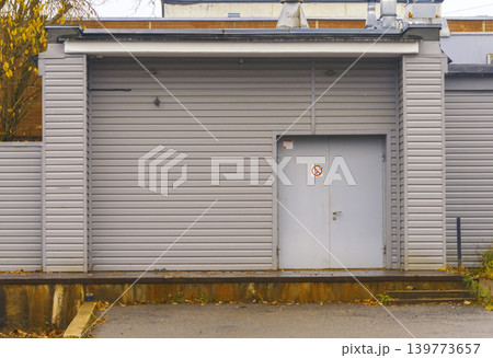 Gray metal shutter with security door. Commercial building entrance featuring metal gate and safety sign 139773657