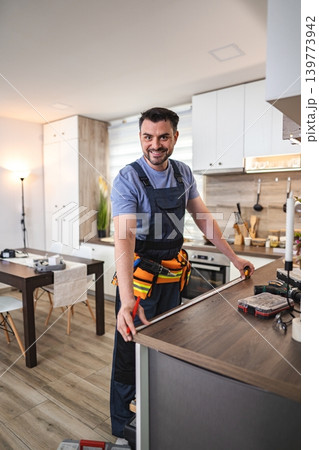 Carpenter taking measurements of kitchen counter in a modern apartment Carpenter taking measurements of kitchen counter in a modern apartment 139773942