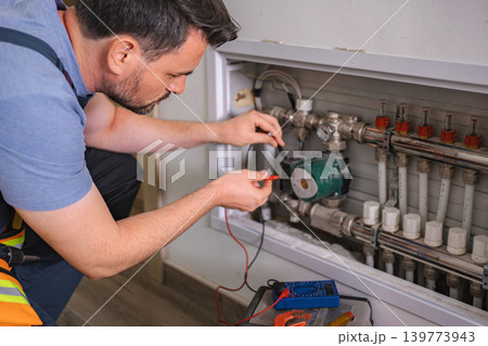 Technician checking underfloor heating pump with multimeter 139773943