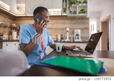 Smiling nurse working from home using laptop and talking on the phone Smiling nurse working from home using laptop and talking on the phone 139773955
