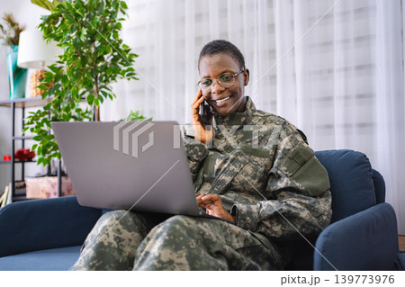 Smiling african american soldier talking on phone and using laptop at home 139773976