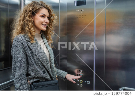 Smiling woman pressing elevator button in office building Smiling woman pressing elevator button in office building 139774004