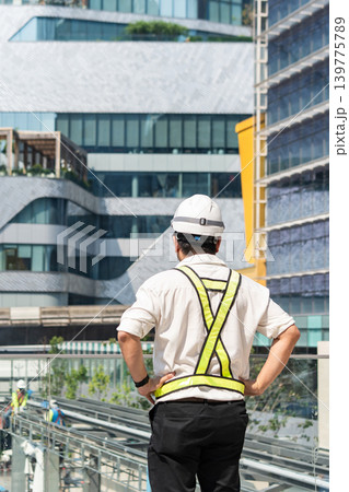 Site engineer standing with hands on waist while observing workers and planning construction operations. Site engineer standing with hands on waist while observing workers and planning construction operations. 139775789