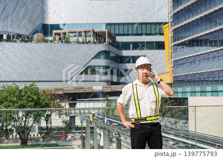 Construction supervisor talking on smartphone while coordinating workers and managing operations at modern construction site. Construction supervisor talking on smartphone while coordinating workers and managing operations at modern construction site. 139775793
