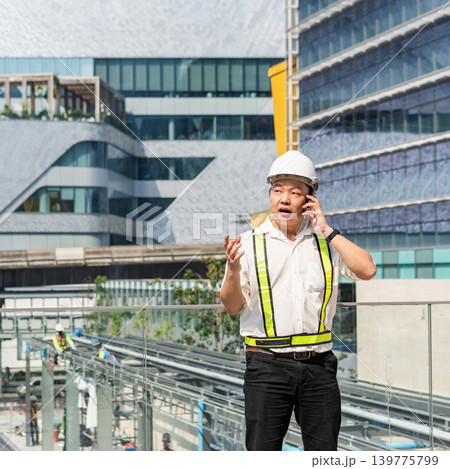 Construction supervisor talking on smartphone while coordinating workers and managing operations at modern construction site. Construction supervisor talking on smartphone while coordinating workers and managing operations at modern construction site. 139775799