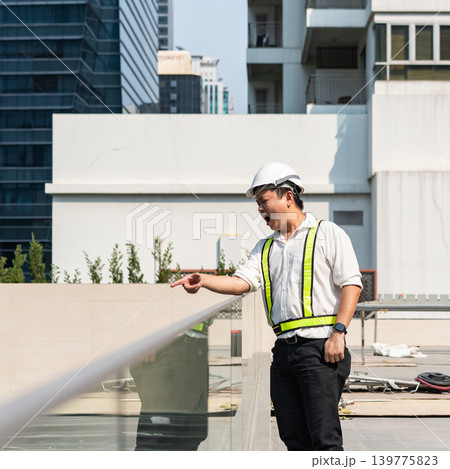 Angry construction supervisor shouting and pointing at workers while controlling operations from upper construction balcony. 139775823