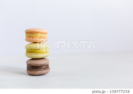 Three French macarons on a white wooden table. Multicolored macarons. White background. Three French macarons on a white wooden table. Multicolored macarons. White background. 139777258