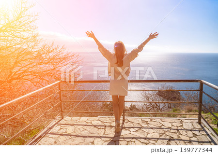 Woman ocean freedom young woman stands on a scenic overlook with arms raised towards the sea at sunrise with copy space Woman ocean freedom young woman stands on a scenic overlook with arms raised towards the sea at sunrise with copy space 139777344