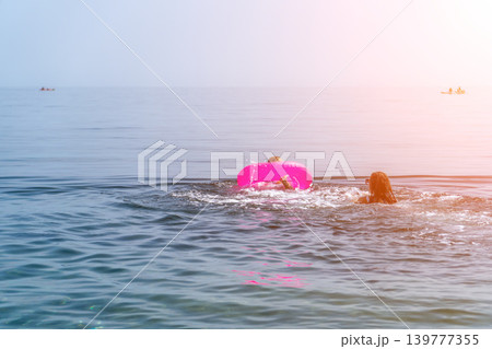 Swimming vacation ocean woman and child playing with a pink inflatable ring in the blue sea water during a sunny summer day Swimming vacation ocean woman and child playing with a pink inflatable ring in the blue sea water during a sunny summer day 139777355