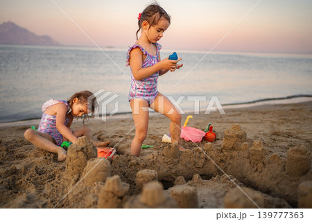 Happy children building sandcastle on Greece beach at sunset 139777363