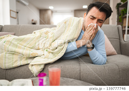 Sick man having a runny nose while lying on a sofa covered with blanket 139777746