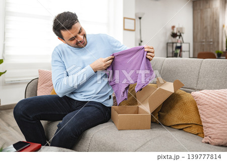 Man opens the cardboard package and looks at the new T-shirt Man opens the cardboard package and looks at the new T-shirt 139777814