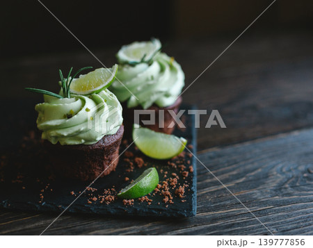 Tasty chocolate cupcake with buttercream icing and lime slices on a wooden table. 139777856