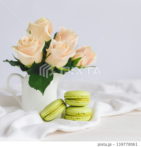 Two light green French macarons with tender roses in a vase on white background. Close up. Pistachio macarons. Two light green French macarons with tender roses in a vase on white background. Close up. Pistachio macarons. 139778061