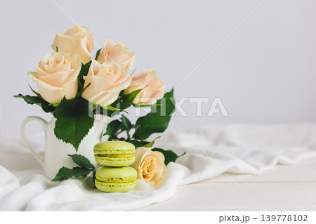 Two light green French macarons with tender roses in a vase on white background. Close up.  Pistachio macarons. 139778102