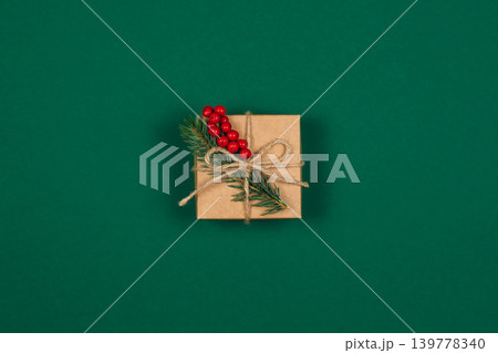 Craft gift box with spruce branch and red berries on green background. Holiday eco-friendly concept. Craft gift box with spruce branch and red berries on green background. Holiday eco-friendly concept. 139778340
