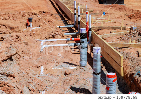 Workers prepare site for new building, installing plumbing fixtures in ground before foundation work begins. Workers prepare site for new building, installing plumbing fixtures in ground before foundation work begins. 139778369