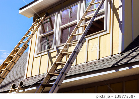 Workers use ladders to reach window on second floor of house during home repair project Workers use ladders to reach window on second floor of house during home repair project 139778387