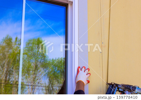 Builder uses nail gun to adjust window trim frame setting is outdoors 139778410