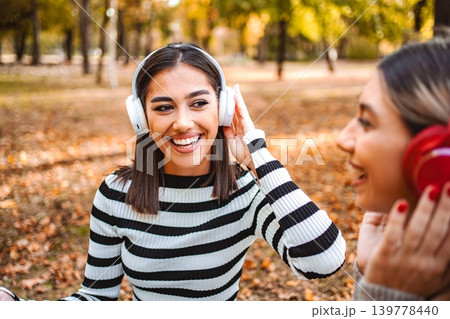 Joyful autumn moments as two girls share music in a vibrant park Joyful autumn moments as two girls share music in a vibrant park 139778440