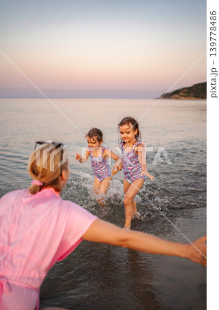 Mother welcoming happy kids playing in sea at sunset Mother welcoming happy kids playing in sea at sunset 139778486