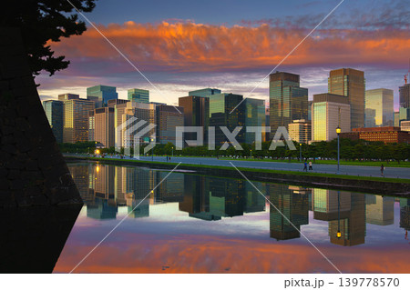 Tokyo, Japan - Oct 1 2024, panoramic view of skyscrapers of Chiyoda district, with a moat in foreground with mirror-like water reflecting buildings and sky, and colorful clouds in sky at sunset, Tokyo 139778570