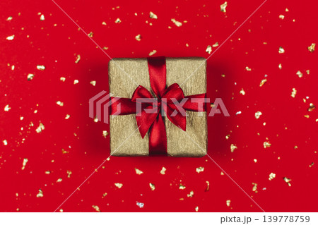 Golden gift box with red bow on the red background with golden sparkles. Golden gift box with red bow on the red background with golden sparkles. 139778759