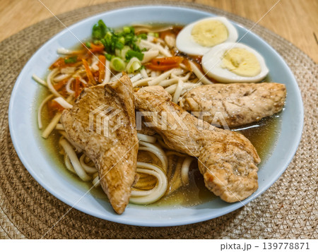 A bowl of noodles rests on a table with fish fillets, boiled eggs, and chopped vegetables. The setting is simple and inviting, perfect for a meal A bowl of noodles rests on a table with fish fillets, boiled eggs, and chopped vegetables. The setting is simple and inviting, perfect for a meal 139778871