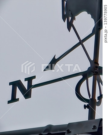 A wind vane shows the direction of the wind with the arrow pointing north against a clear sky. This takes place on a rooftop in the late afternoon A wind vane shows the direction of the wind with the arrow pointing north against a clear sky. This takes place on a rooftop in the late afternoon 139778905