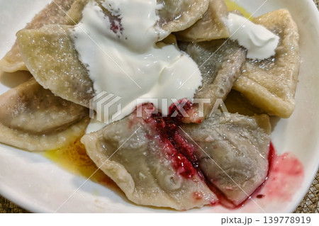 Dumplings are served with dollops of sour cream and berry sauce on a white plate in a cozy kitchen during dinner time Dumplings are served with dollops of sour cream and berry sauce on a white plate in a cozy kitchen during dinner time 139778919