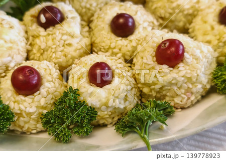 A plate holds small round food items covered in sesame seeds, topped with red grapes, and garnished with parsley during a casual evening gathering at a home 139778923
