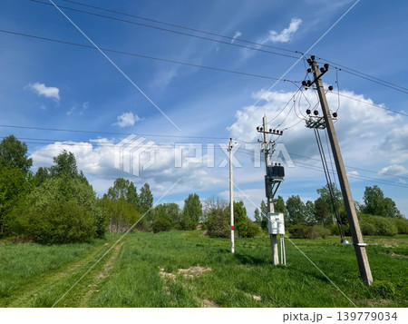 Electrical utility poles and power lines across rural landscape under blue cloudy summer sky Electrical utility poles and power lines across rural landscape under blue cloudy summer sky 139779034