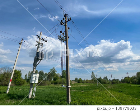 Rural electricity transmission lines and utility poles across green landscape under cloudy sky Rural electricity transmission lines and utility poles across green landscape under cloudy sky 139779035
