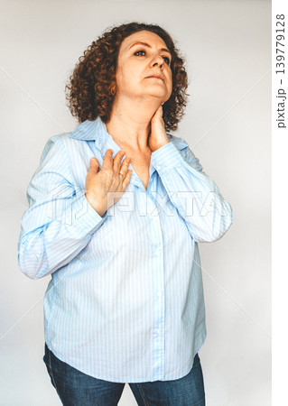 Middle-aged woman in blue shirt touching her neck and chest showing discomfort and concern 139779128