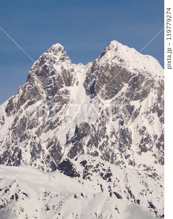 Vertical view the snow-capped peaks pierce a bright blue sky. Mount Ushba in Svaneti, Georgia. Vertical view the snow-capped peaks pierce a bright blue sky. Mount Ushba in Svaneti, Georgia. 139779274