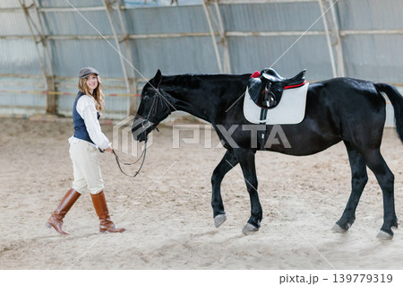 Woman exercising black horse in riding arena Woman exercising black horse in riding arena 139779319