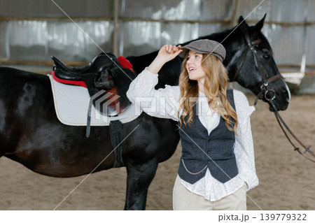 Young woman confidently posing with black horse indoors Young woman confidently posing with black horse indoors 139779322
