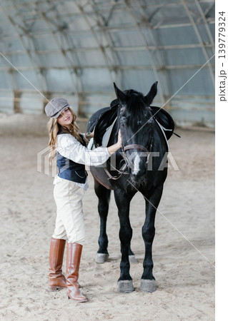 Woman with flat cap and black horse in riding arena Woman with flat cap and black horse in riding arena 139779324