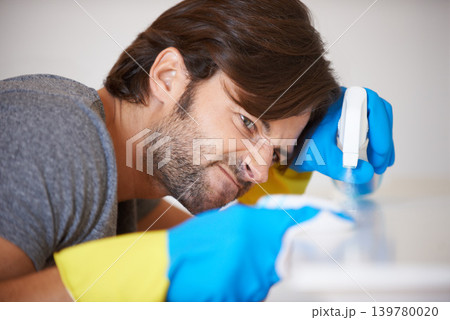 Man, face and spraying surface for housekeeping, hygiene or disinfection on furniture or table at home. Male person, maid or cleaner checking dirty spots for wiping, bacteria or germ removal at house Man, face and spraying surface for housekeeping, hygiene or disinfection on furniture or table at home. Male person, maid or cleaner checking dirty spots for wiping, bacteria or germ removal at house 139780020
