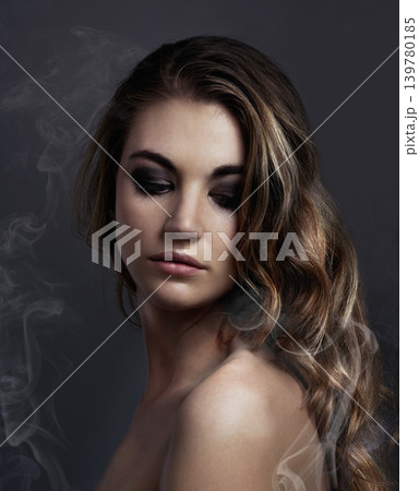 Woman, eyeshadow and makeup, beauty and smoke with hair, cosmetics and balayage on grey background. Serious model, edgy with haircare and vapor, cosmetology and skin with mist or fog in studio 139780185