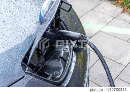 Electric car connects to charging point at station while rain falls on the surface. The location is busy and modern 139780252